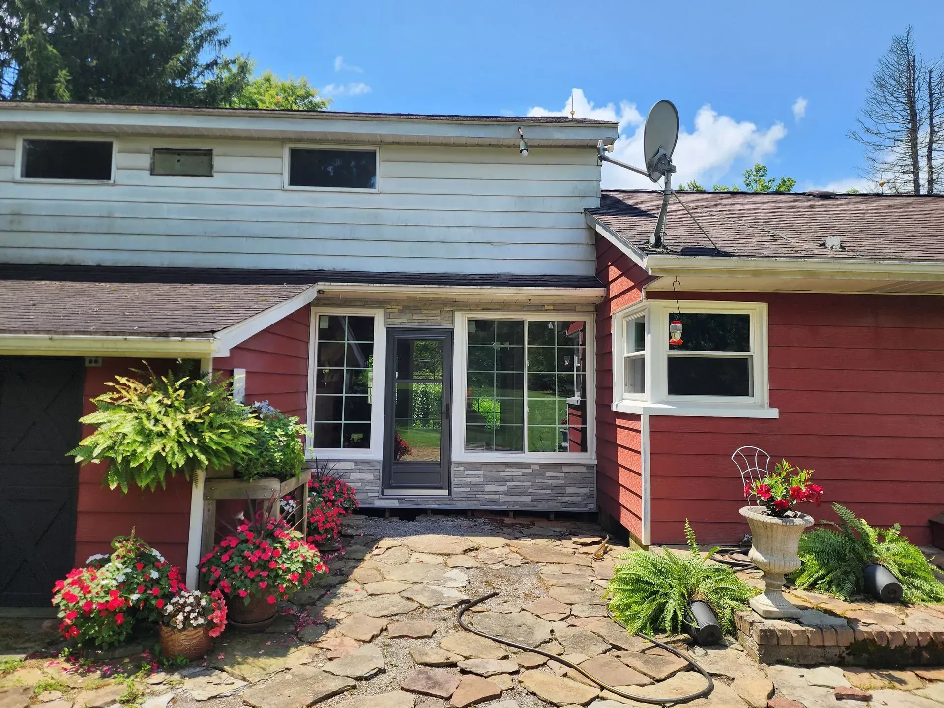 Red two-story house with white upper siding, stone walkway, and flower planters by the front entrance