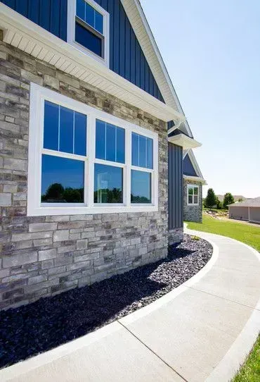 Modern house exterior with stone siding, blue trim, large windows, and a curved concrete walkway.
