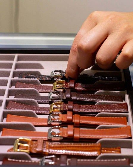Hand arranging brown leather watch straps in a display tray