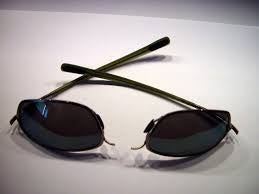 Oval dark sunglasses with thin black arms crossed on a white surface