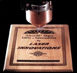 Laser engraving on a wooden plaque with “Awards Signs Gifts & Specialties” and “Laser Innovations” text
