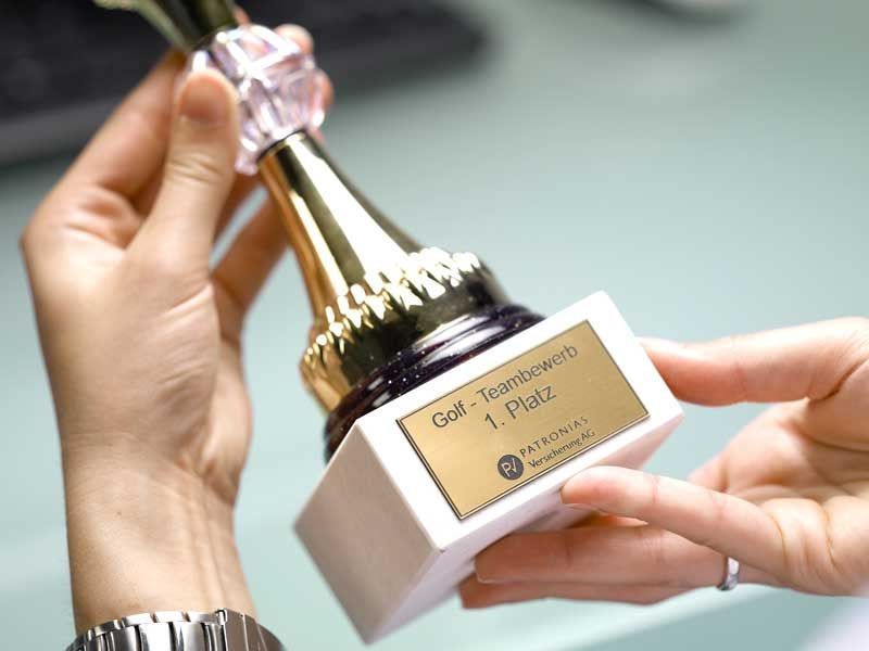 Hands holding a small gold-and-white trophy with a pink gem-like top and label plaque