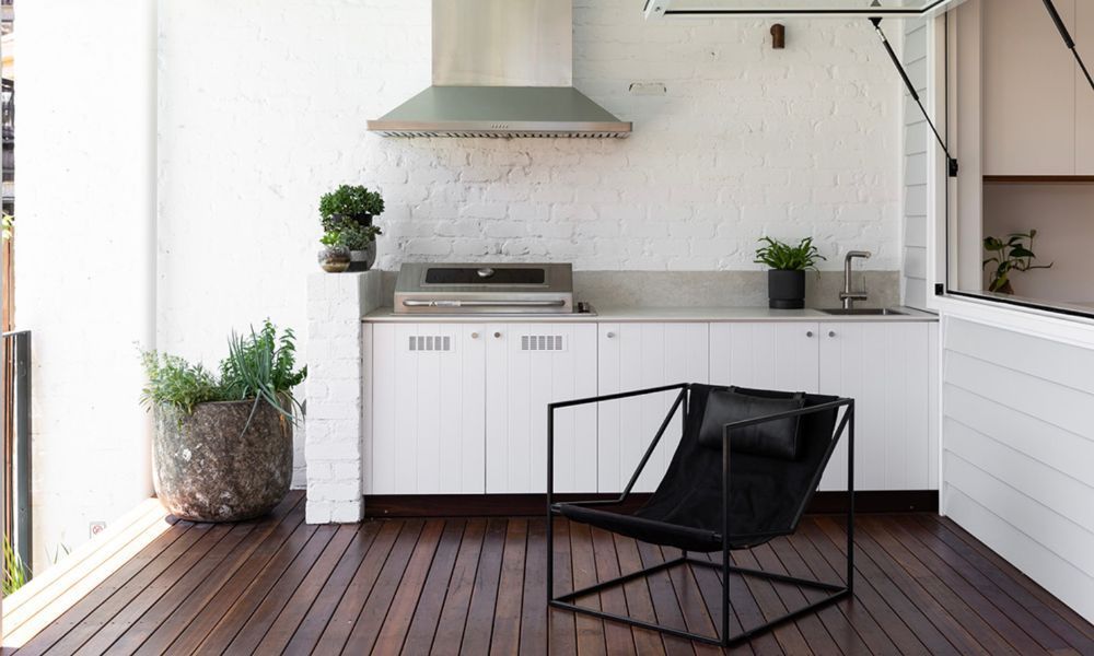 A Black Chair is Sitting on a Wooden Deck Next to a Kitchen — QBC Constructions In Pacific Avenue, QLD