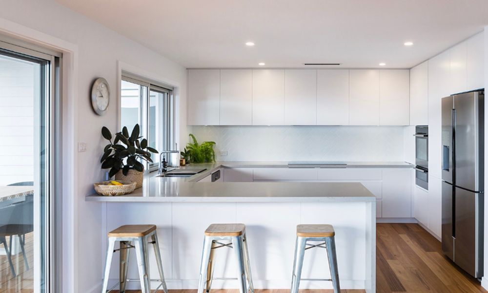 A Kitchen With White Cabinets and Stools and a Clock — QBC Constructions In Gerringong, NSW
