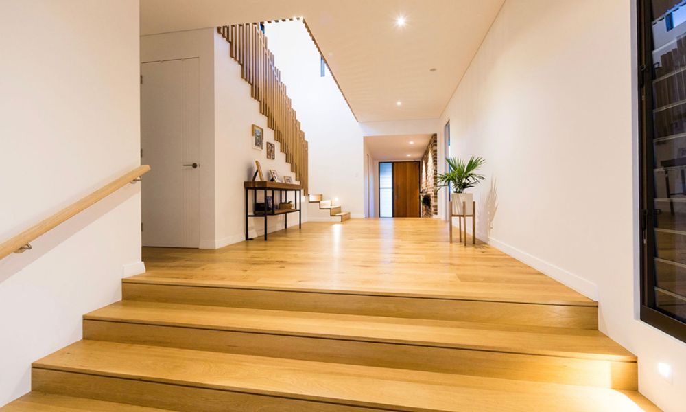 A Hallway With Wooden Stairs Leading Up to a Staircase — QBC Constructions In South Coast, NSW