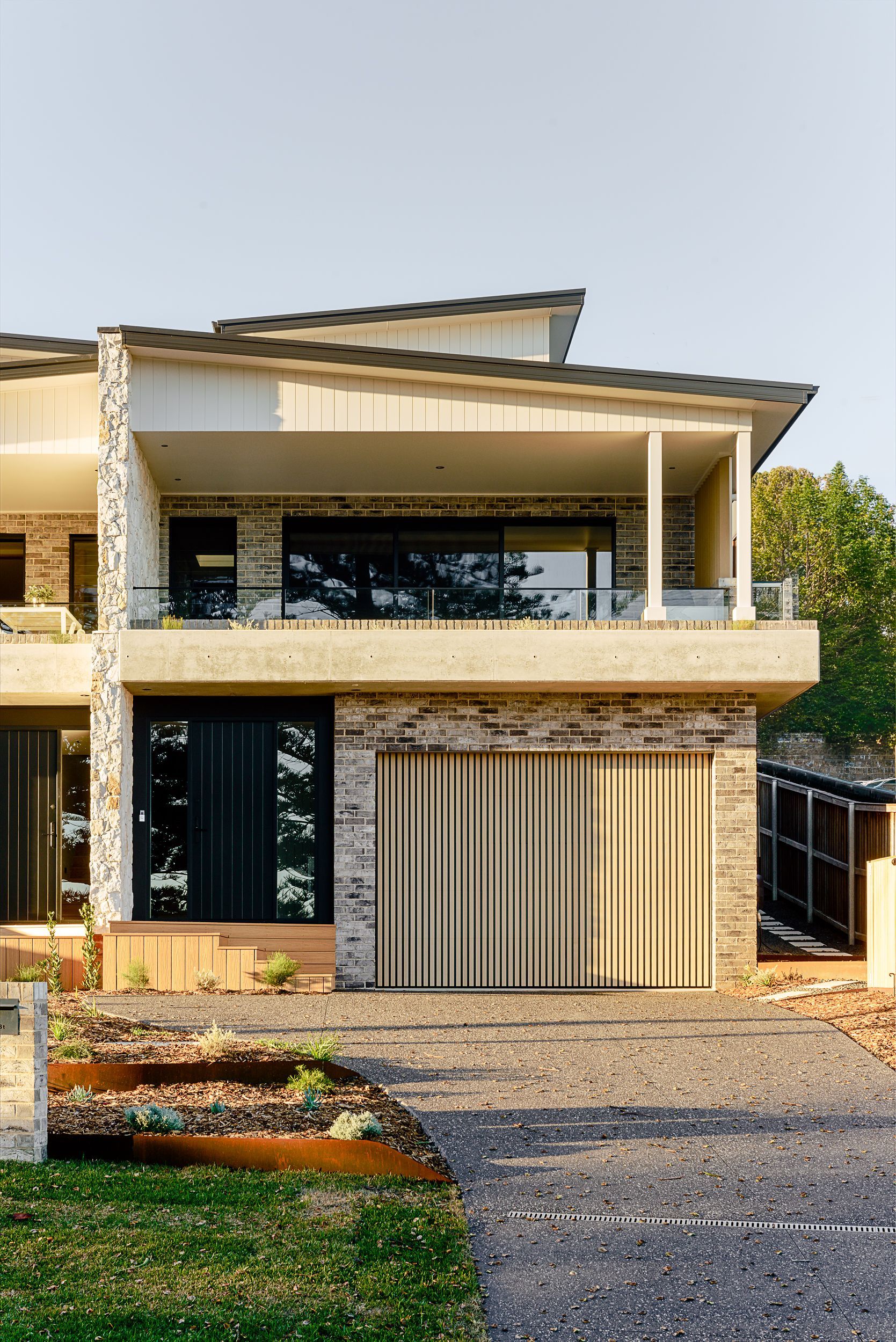 Modern two-story house with stone accents, large windows, and a gated driveway under a slanted roof  — QBC Constructions In Berry, NSW