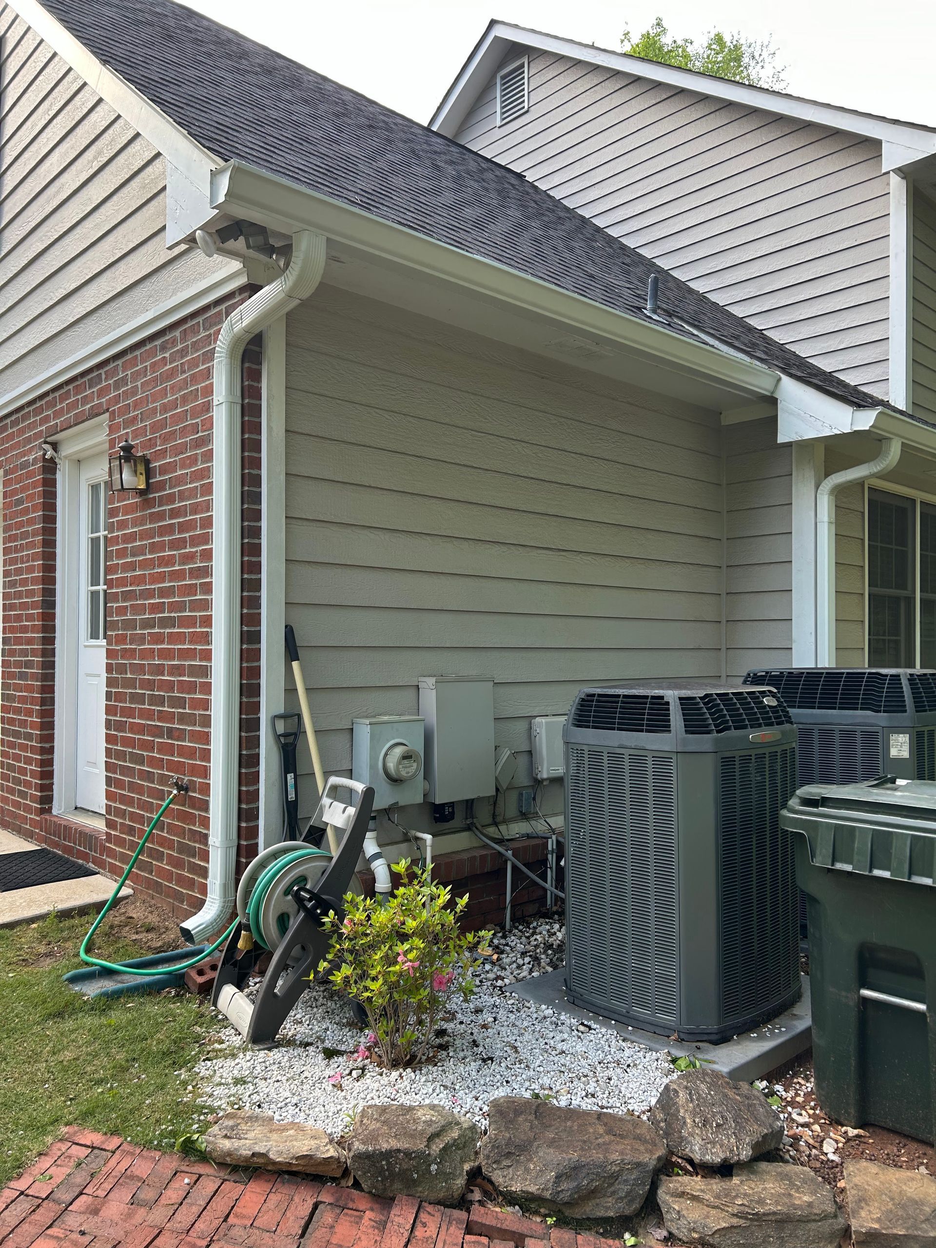 Side view of a house exterior with HVAC units, utility equipment, and landscaping stones near the foundation
