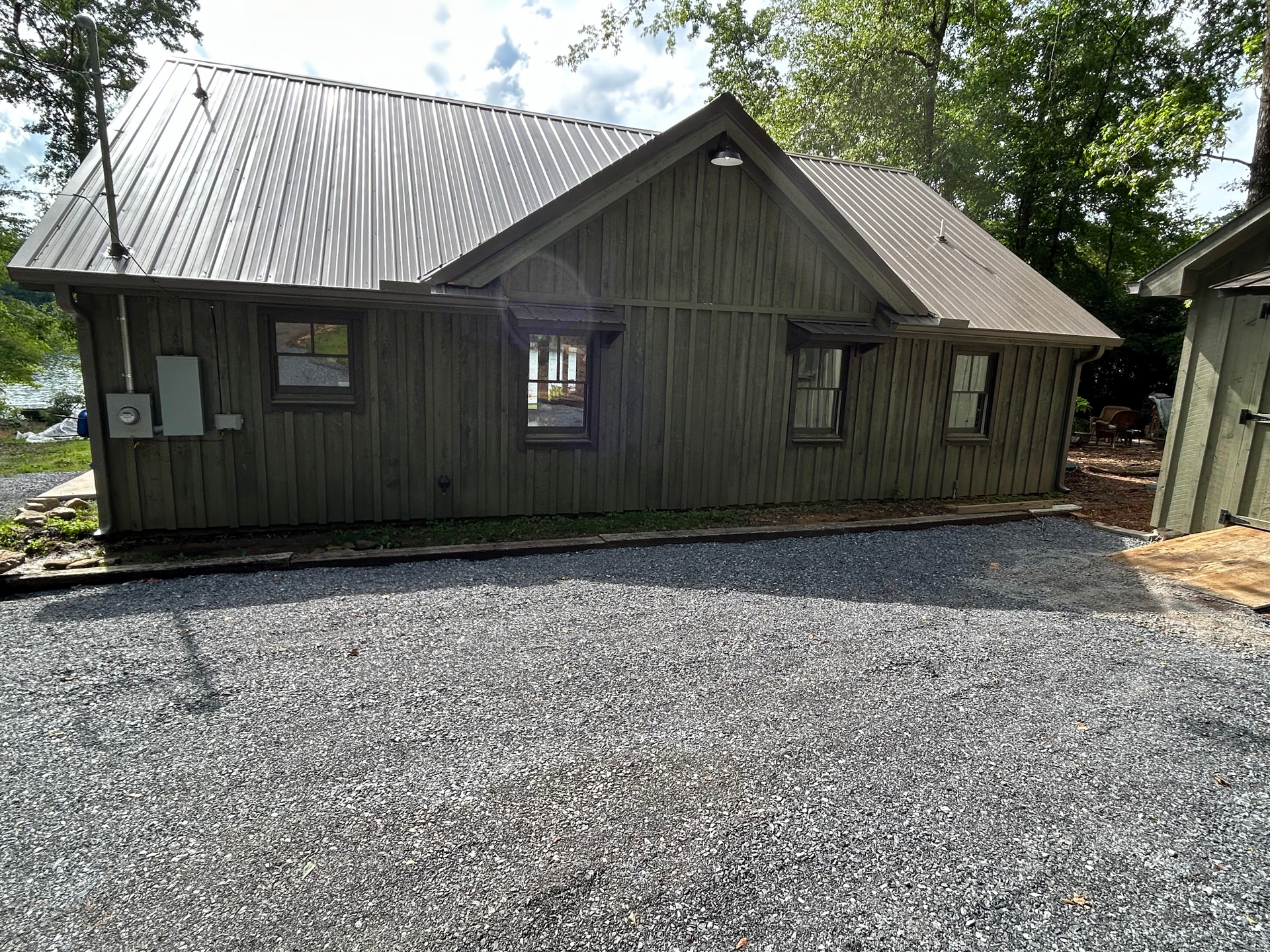 Small rustic cabin with metal roof and gravel driveway surrounded by trees
