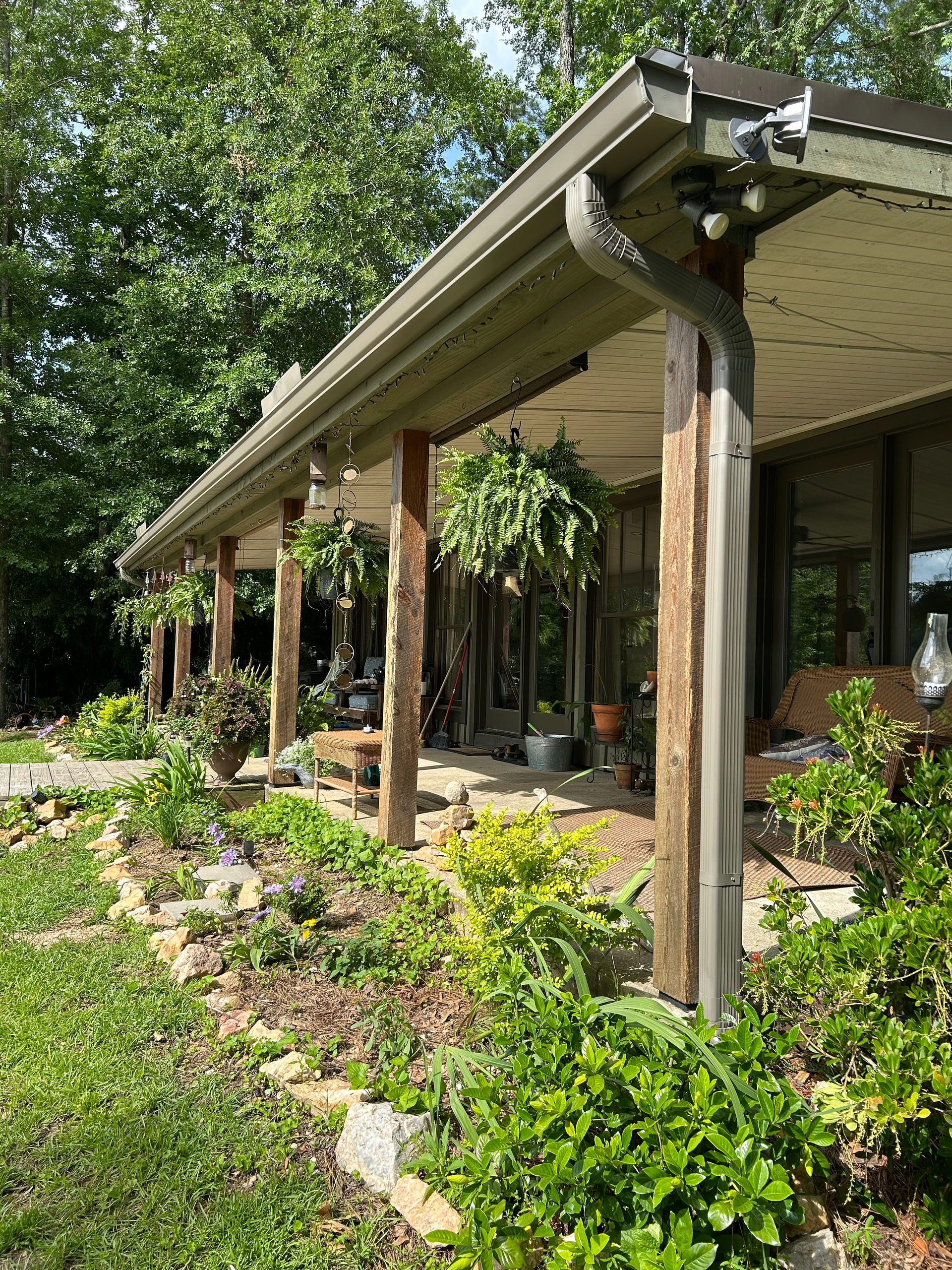 Wooden porch with columns beside a lush garden and trees in bright daylight