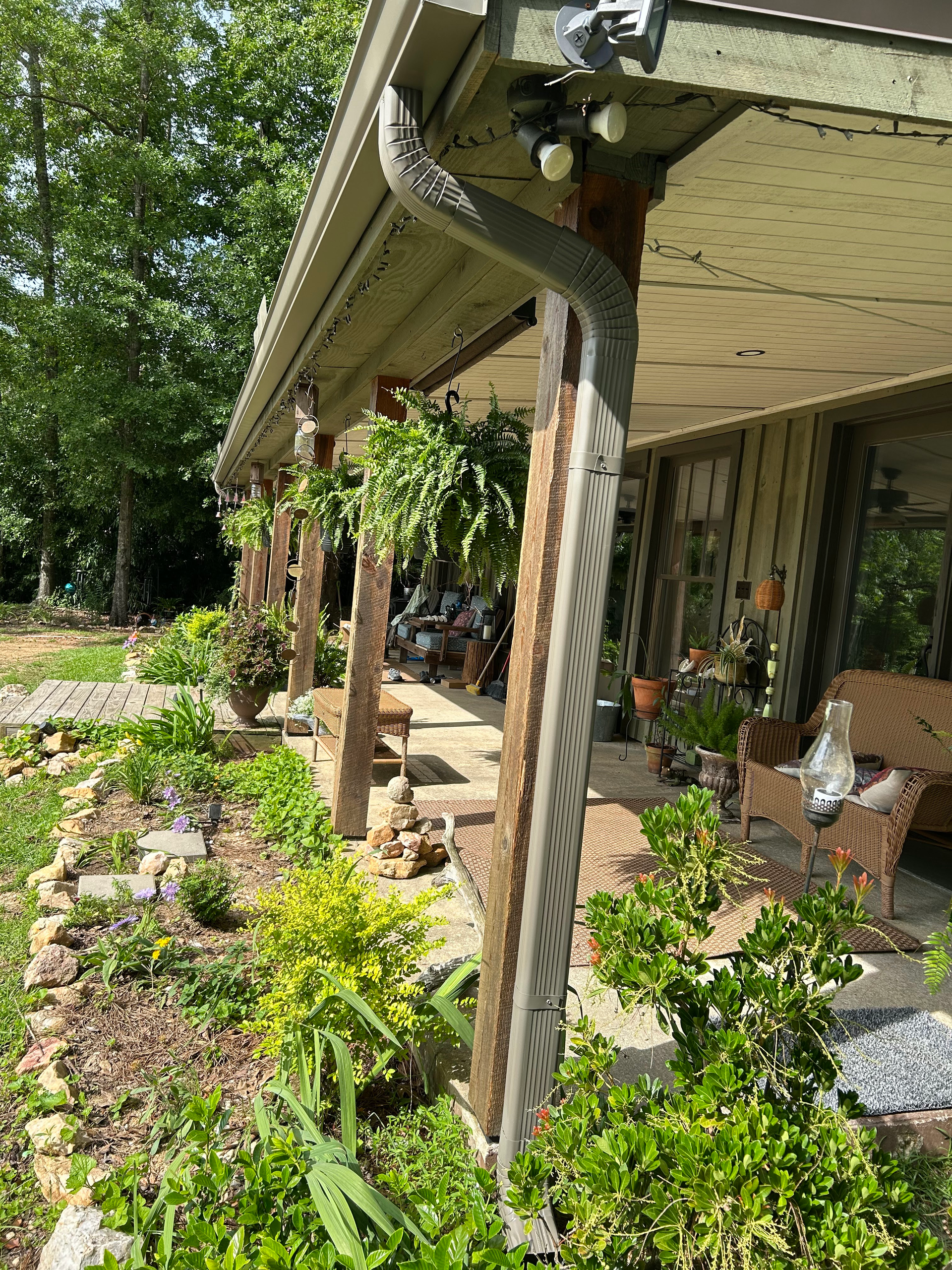Garden-lined porch with hanging plants and a vine-covered post beside a brick house