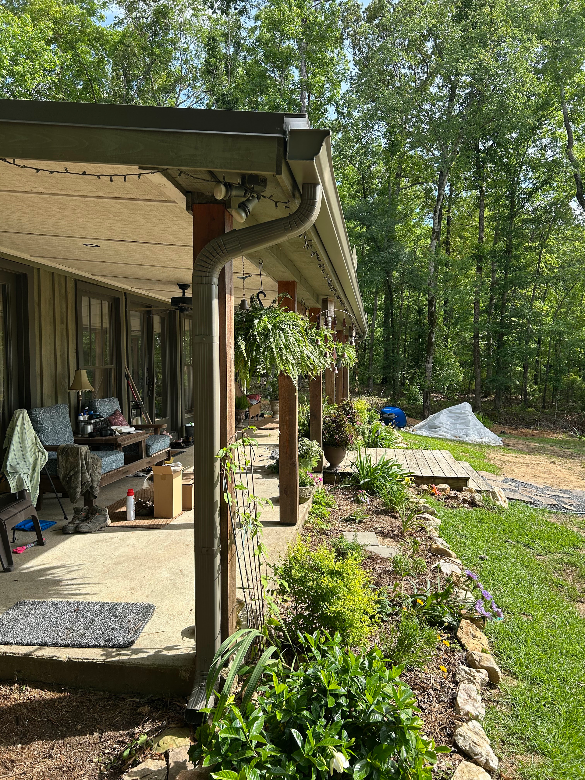 Porch with rocking chairs and potted plants beside a rocky garden and green trees