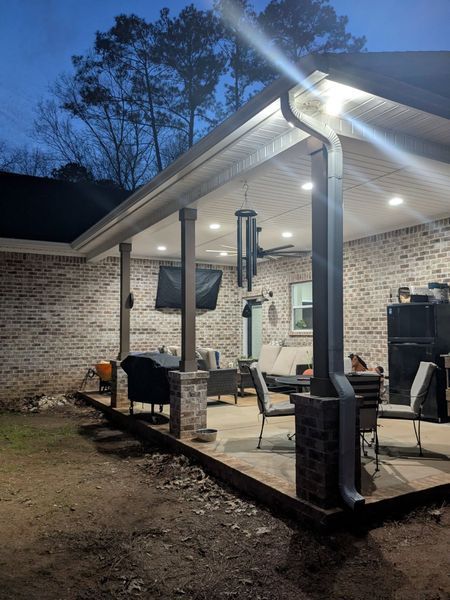 A covered patio with a television and a grill is lit up at night.