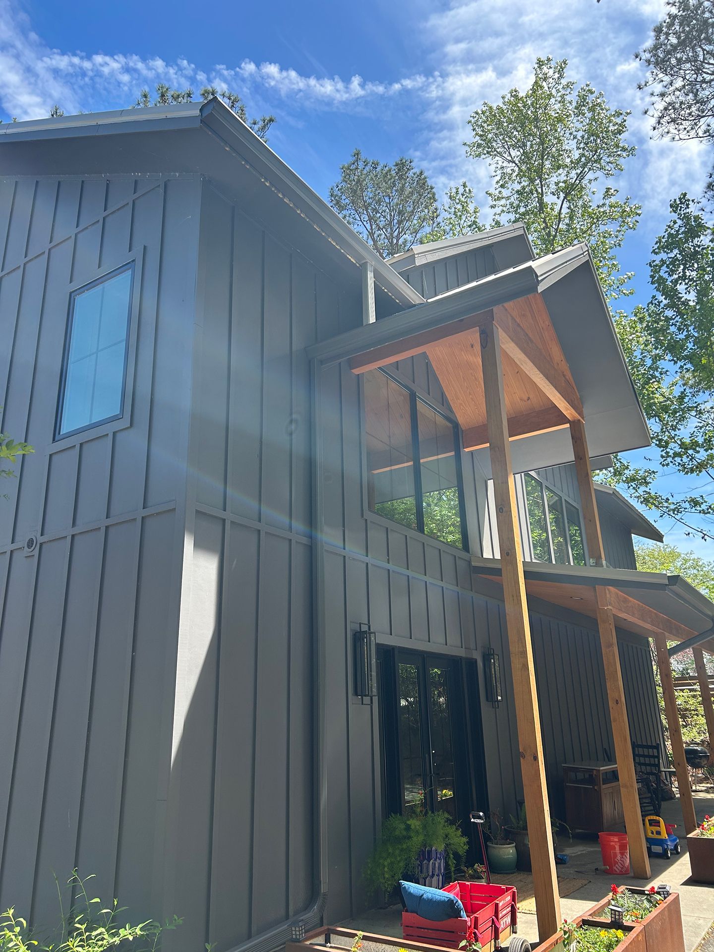 Gray two-story house with wood porch supports and blue sky above, view from the yard