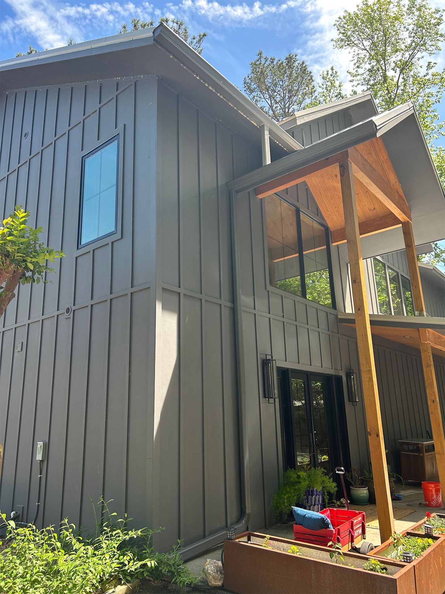 Modern gray house exterior with tall windows, slanted roof, and a small porch with potted plants
