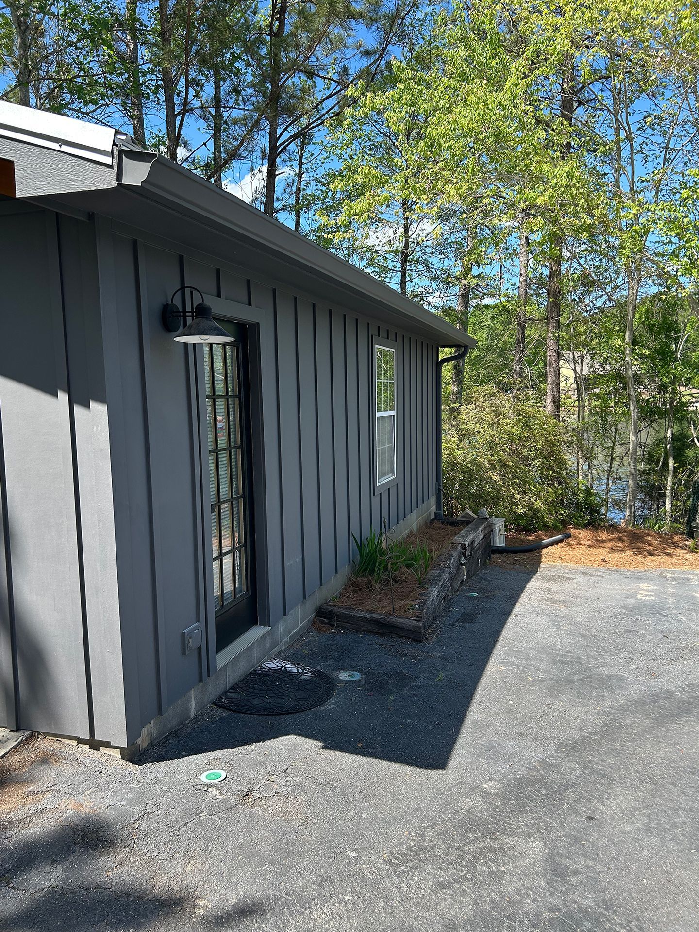 Gray house exterior with gravel driveway, trees, and a screened door by the side wall