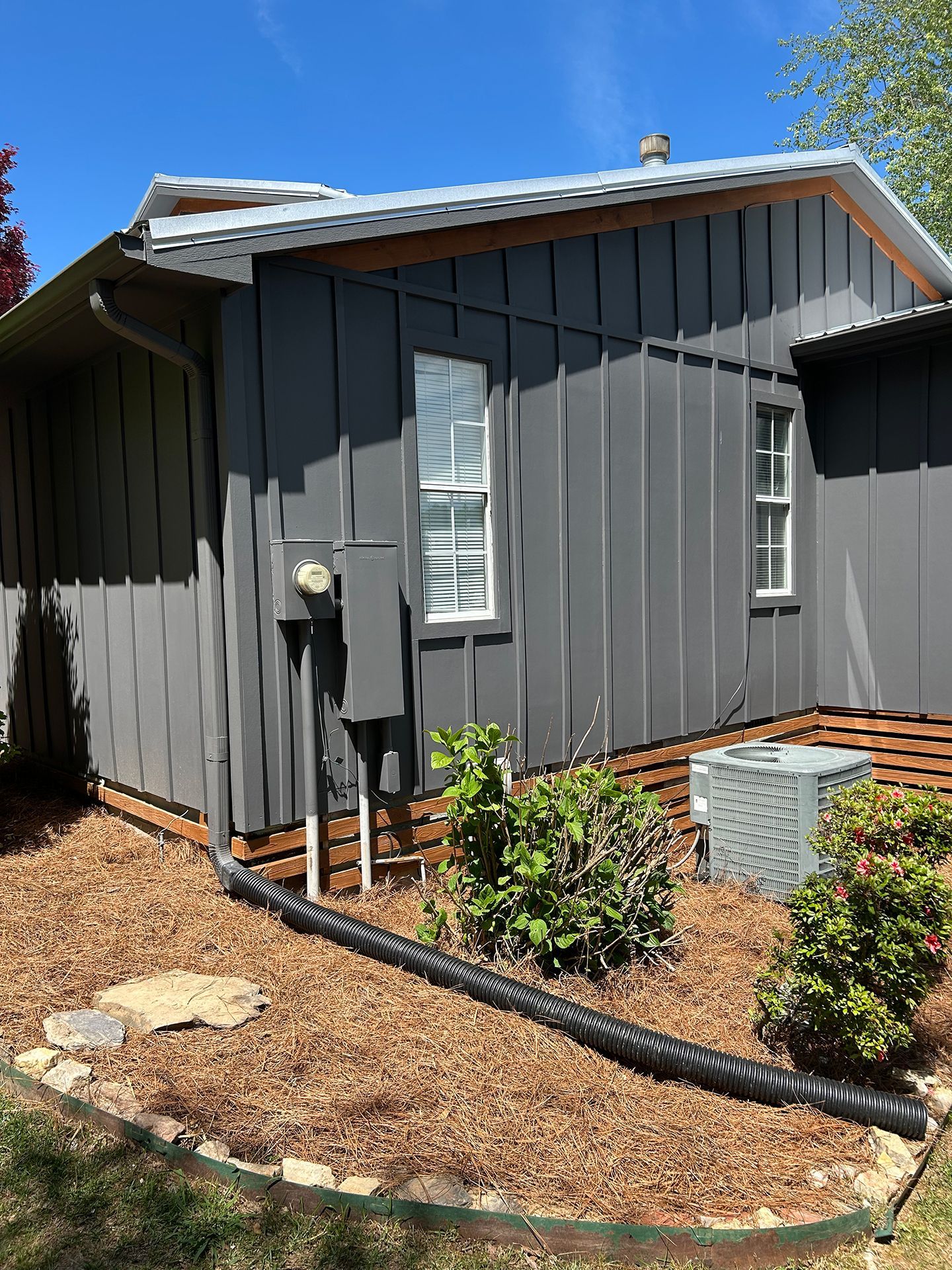 Gray house exterior with white shutters, utility box, and mulch landscaping under a blue sky
