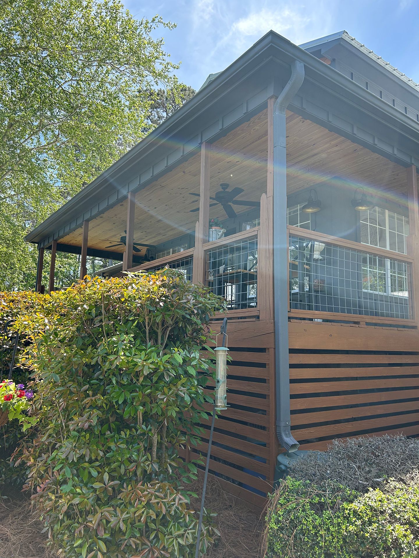 Screened porch on a wooden house with a metal roof, viewed from the garden amid trees and shrubs
