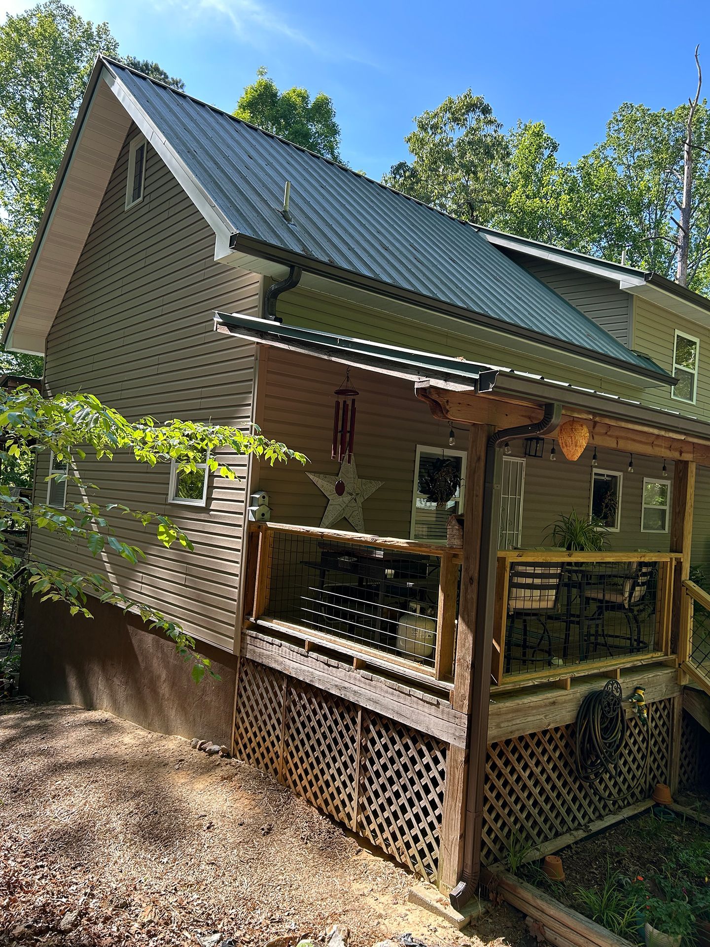 Wood-sided cabin with green metal roof and covered porch in a wooded area