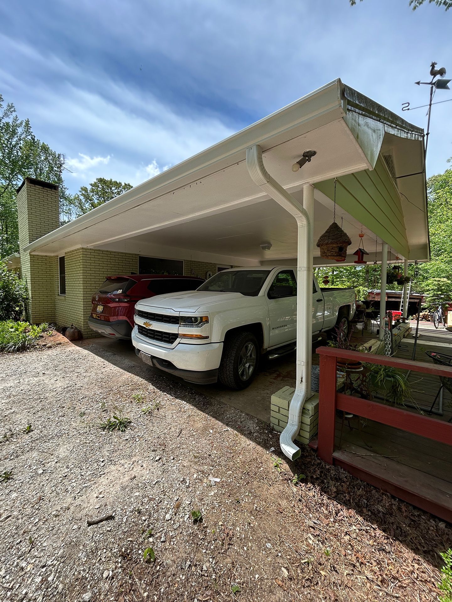 White SUV parked under a beige carport beside a red railing and gravel driveway.