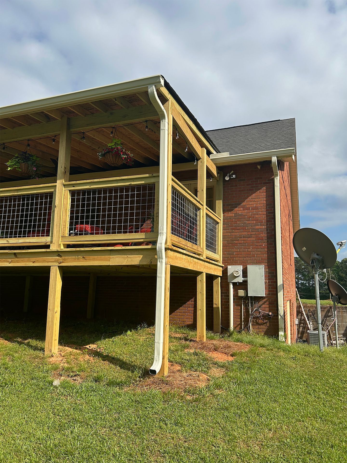 Wooden deck beside a brick house, with black railing panels and a satellite dish in a grassy yard.