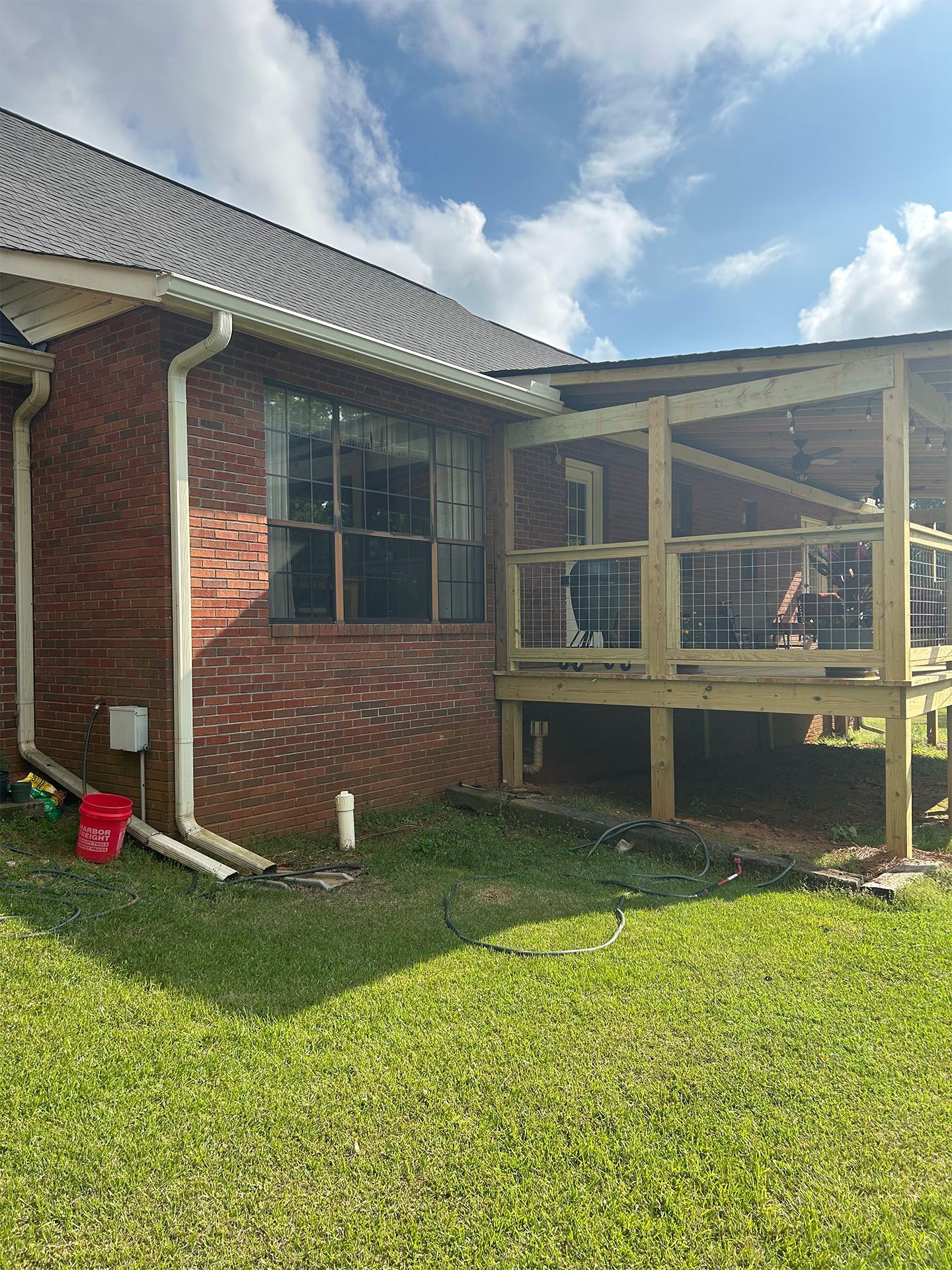 Brick house with a screened porch and wooden deck extension, set in a grassy yard under a partly cloudy sky
