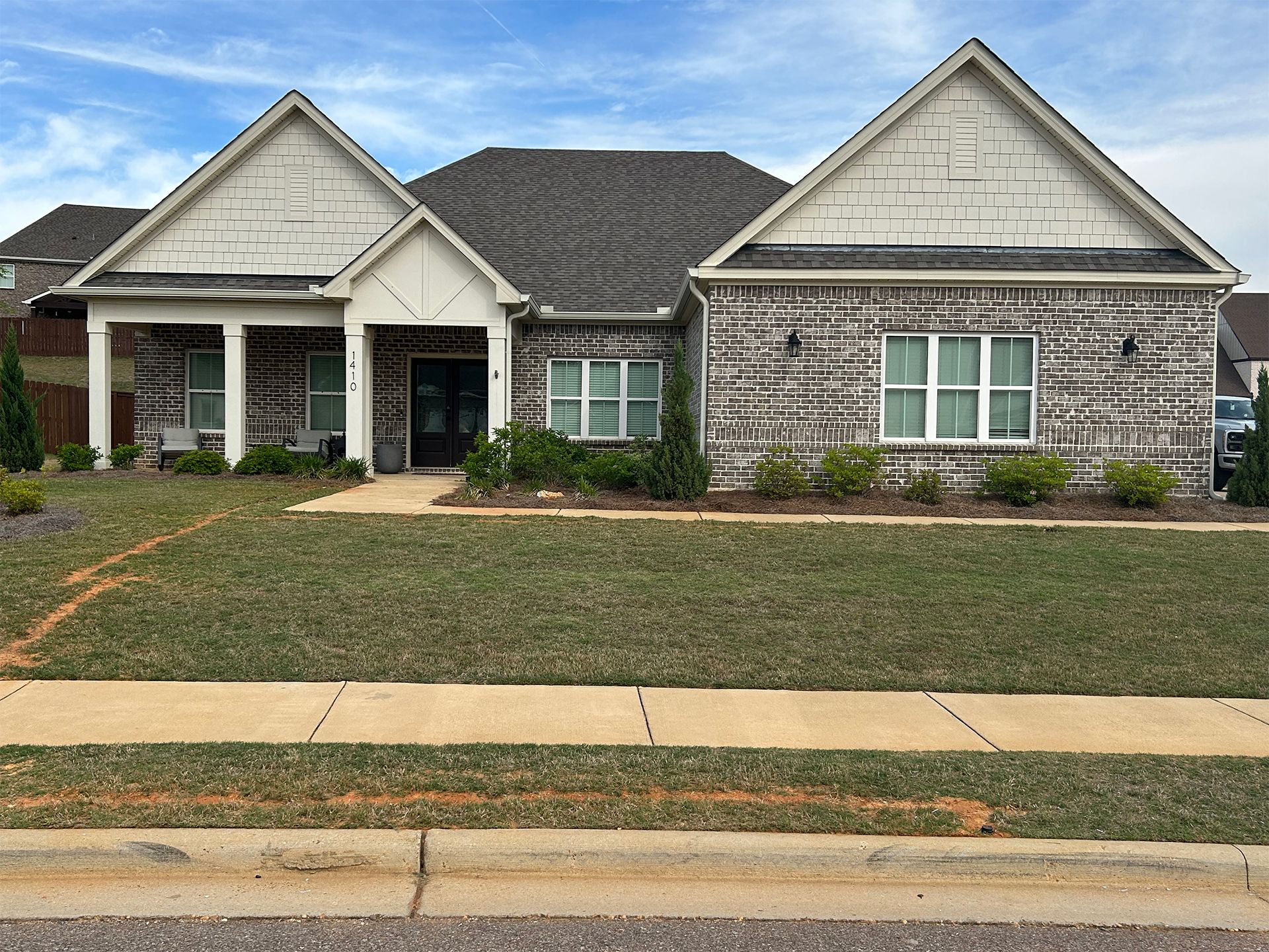 Suburban single-story house with gray siding, white trim, and a front lawn beside a sidewalk