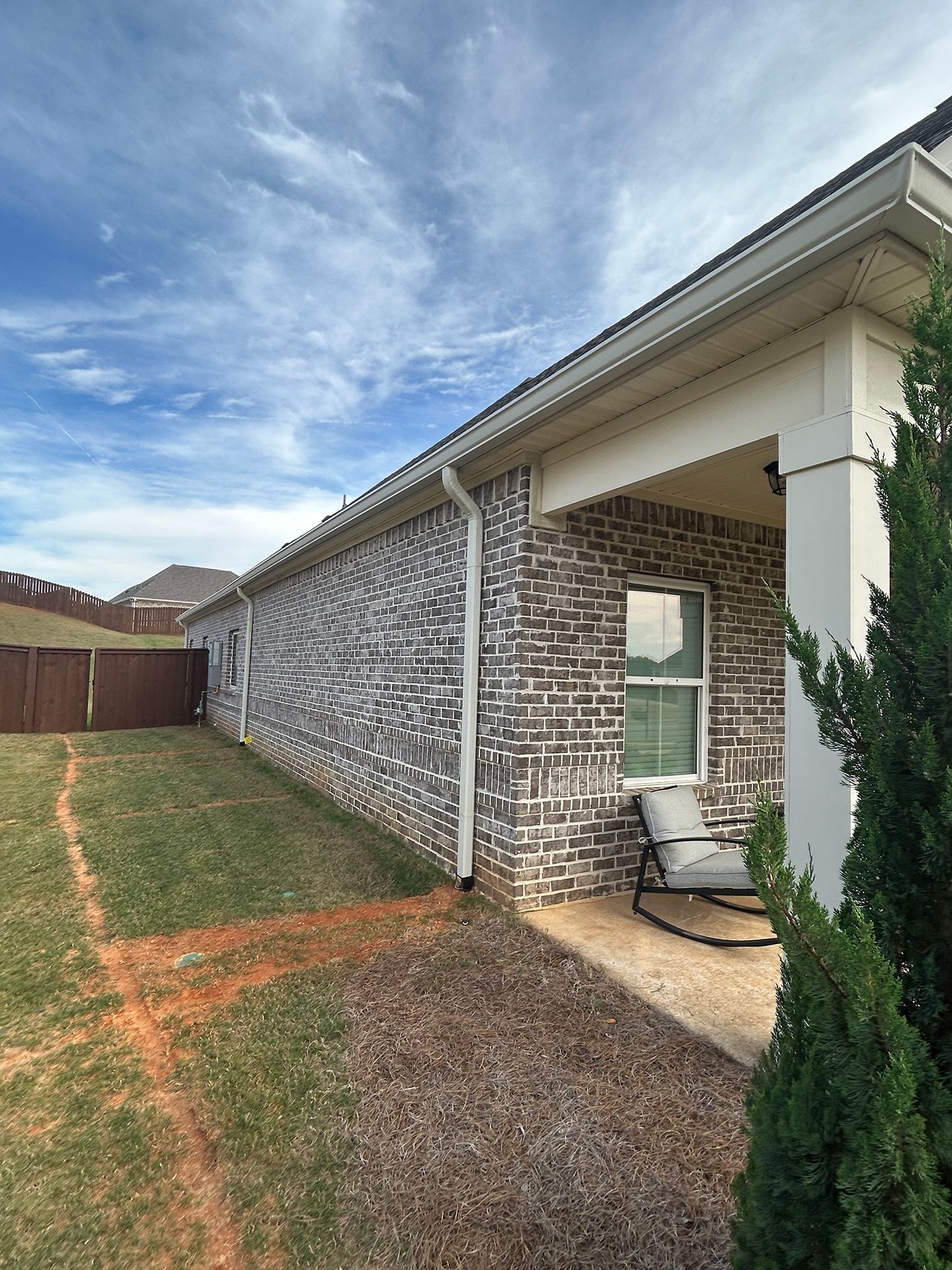 Brick house side yard with brown grass, a covered patio, and a cloudy sky