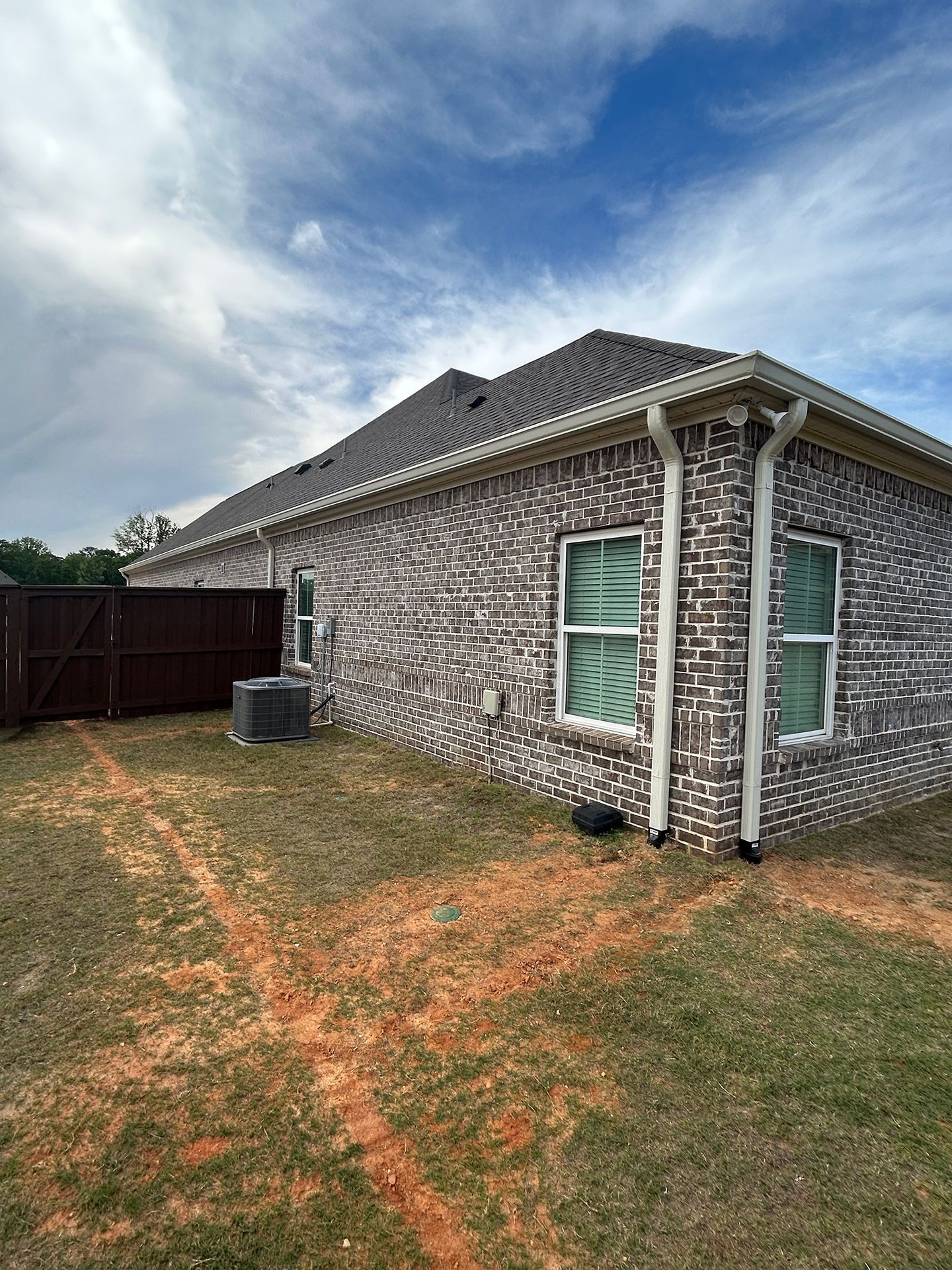 Backyard view of a brick house with a gray roof, windows, fence, and cloudy sky