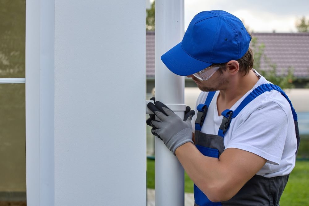 A man in a blue hat and overalls is working on a white pipe.