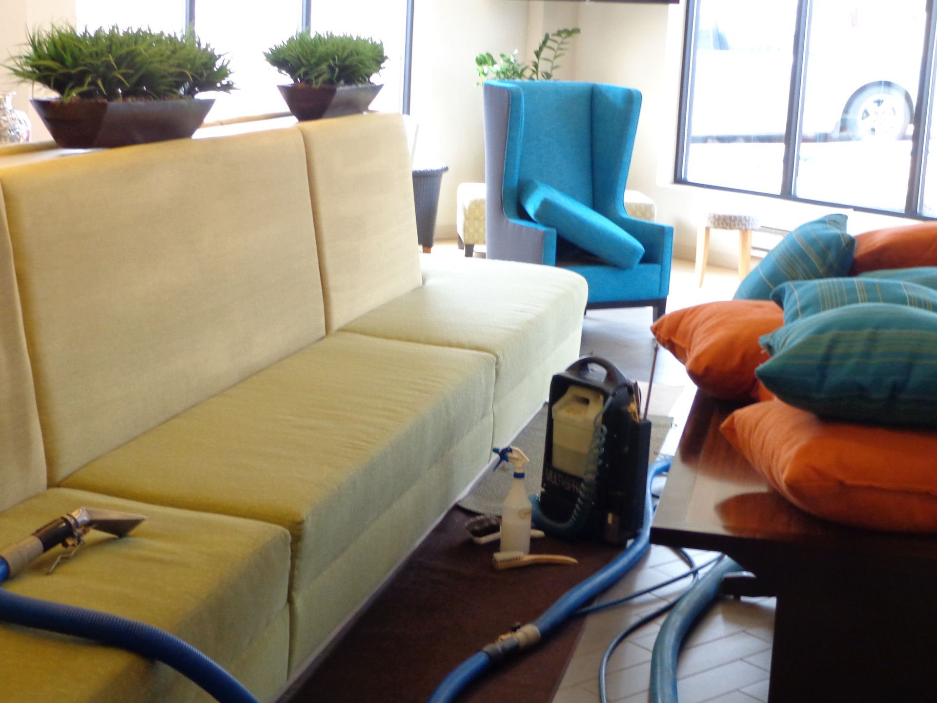 Person in yellow gloves cleaning a gray sofa with a handheld upholstery cleaner.