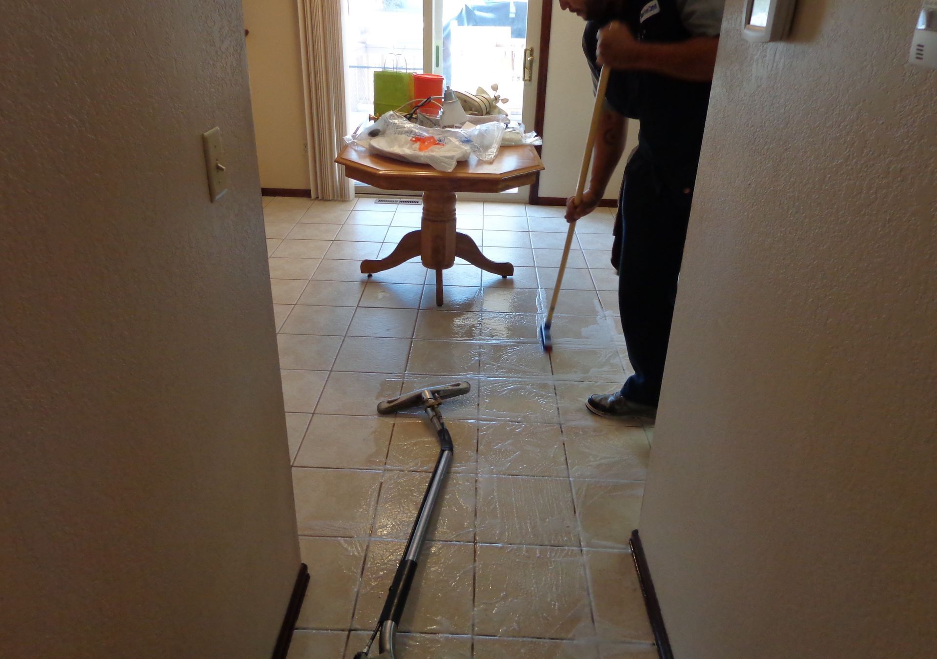 Gloved hand sprays a checkered tile floor with a hose, cleaning the surface.