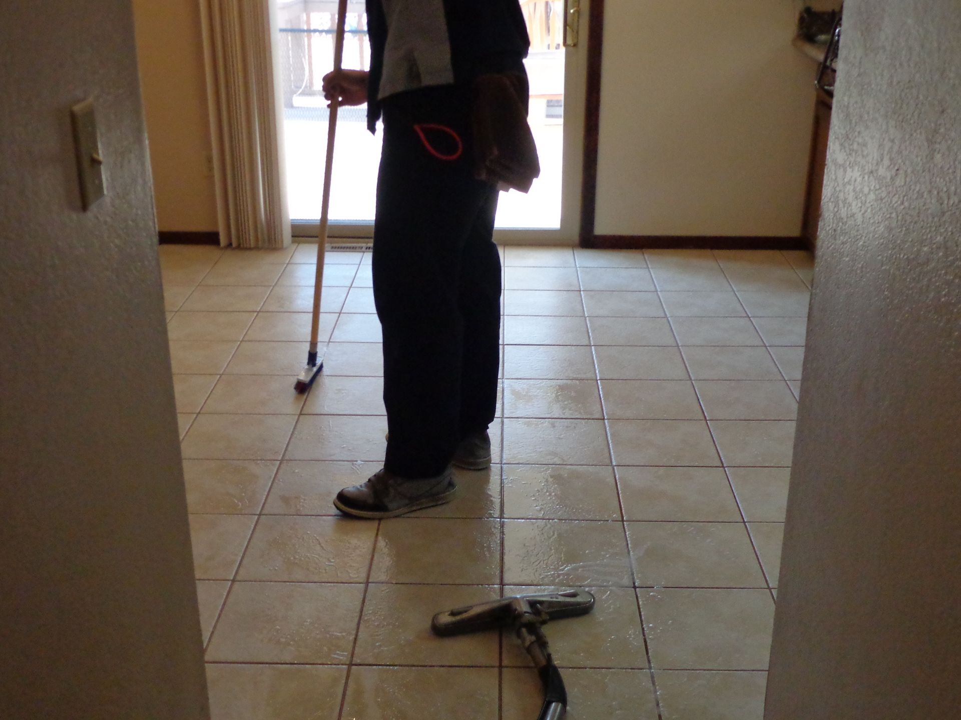 A professional cleaner uses a floor squeegee to dry a tiled floor in a residential living area.