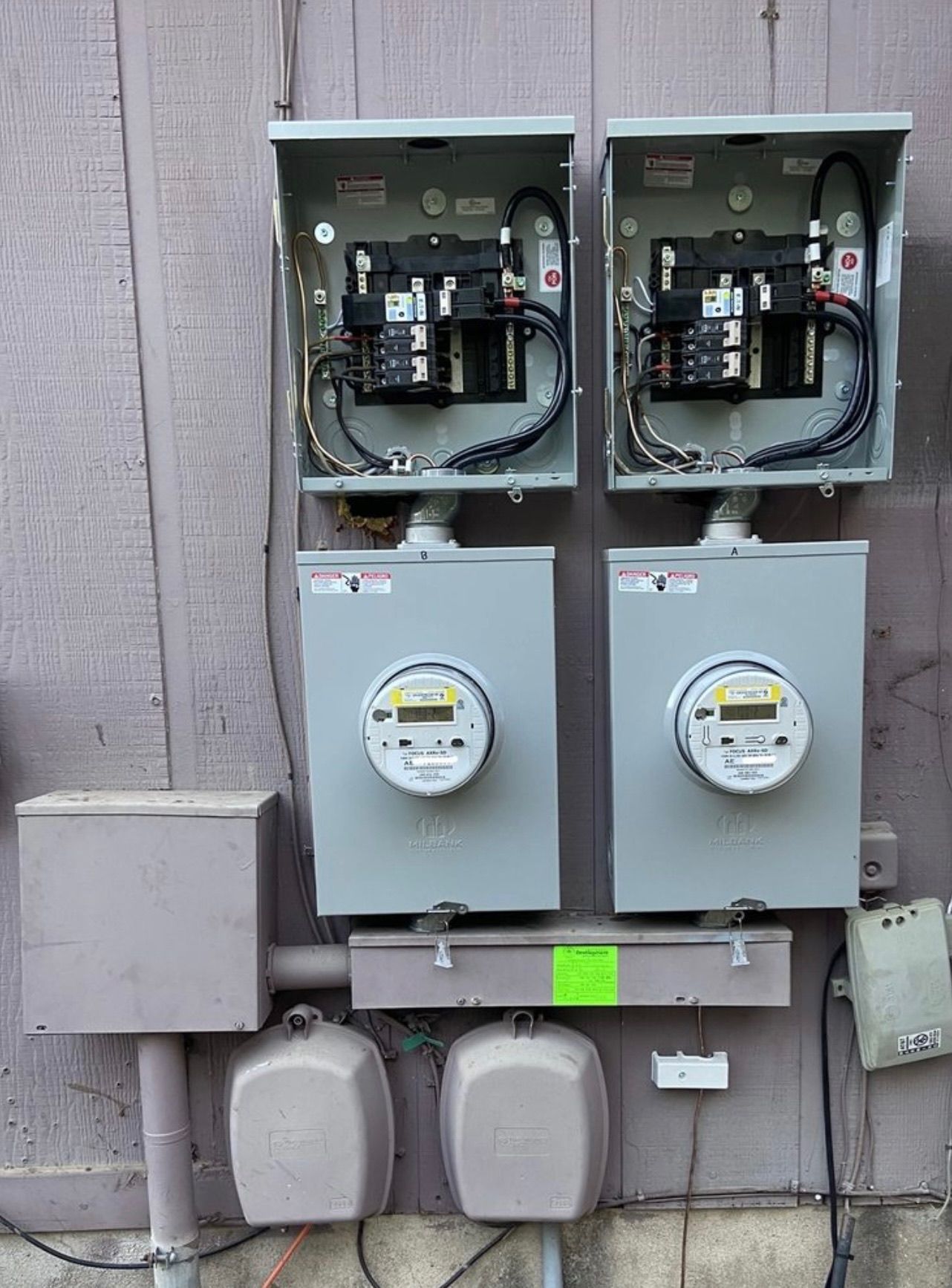 Electrical meters and breakers mounted on a wooden exterior wall.