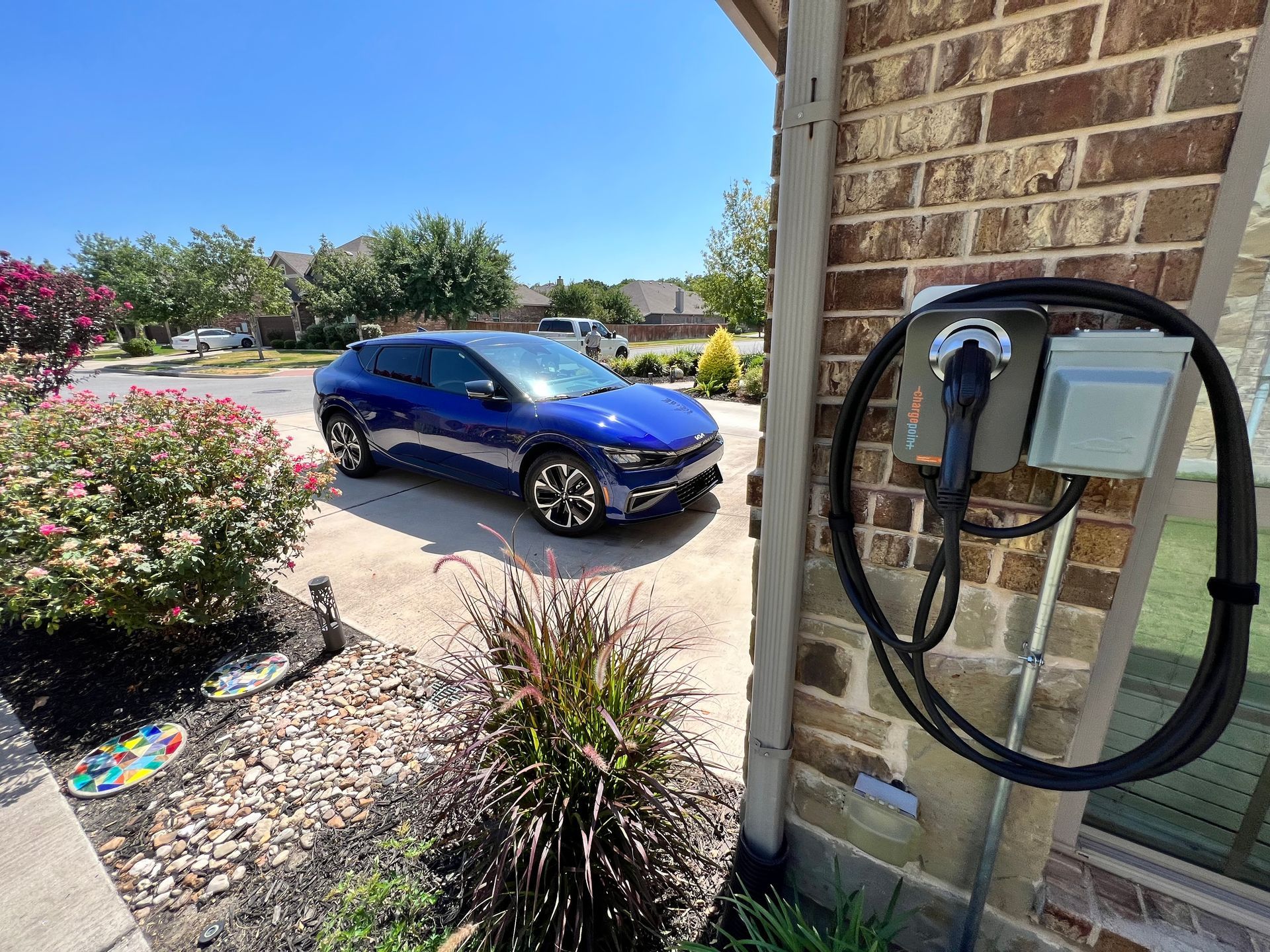A blue electric car parked in a driveway next to a home charging station, sunny day.