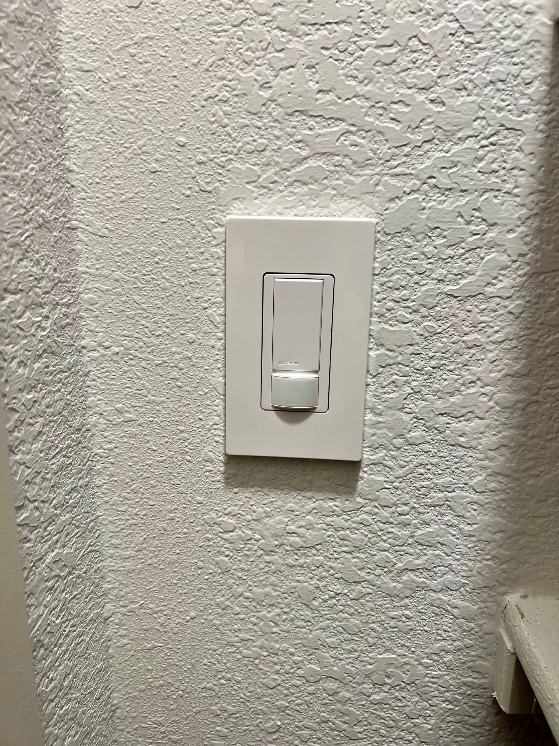 White light switch on a textured gray wall. The switch is rectangular with a rocker.