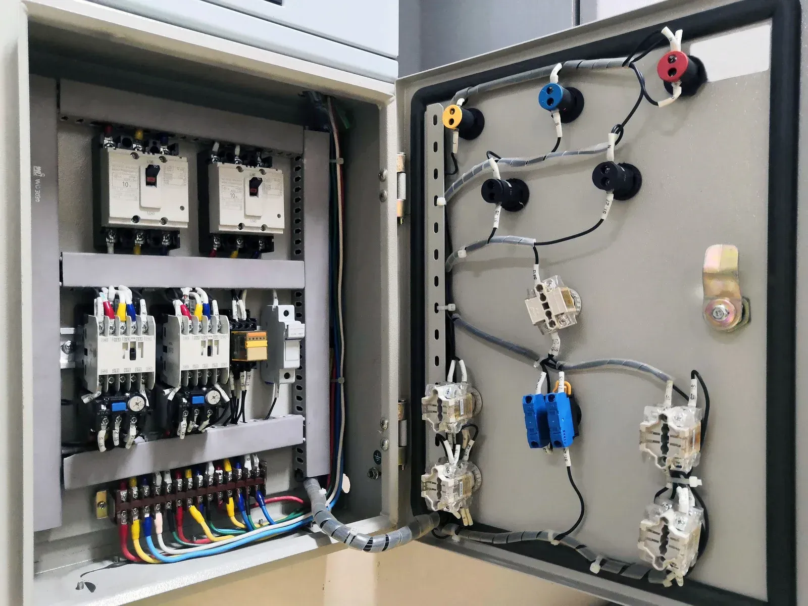 An open electrical control panel with wires, circuit breakers, and other components.