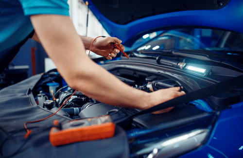 Mechanic working under the hood of a blue car with tools in a garage