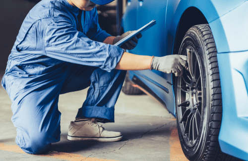 Mechanic in blue coveralls checking a car tire with a tablet in a garage