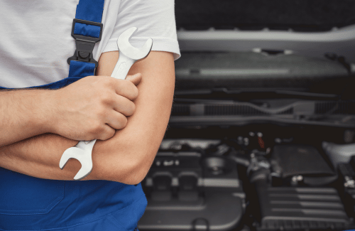 Mechanic in blue overalls holding a wrench in front of an open car engine bay