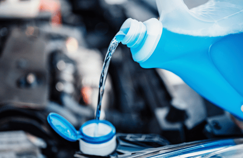 Blue windshield washer fluid being poured into a car reservoir under the hood