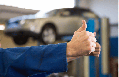 Thumbs-up in blue work sleeve with a car on a lift in the background.