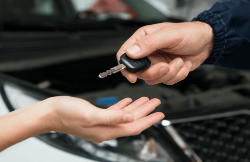 Car key being handed over above an open car hood