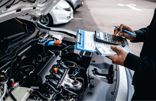 Mechanic checking engine bay and clipboard beside a white car with hood open