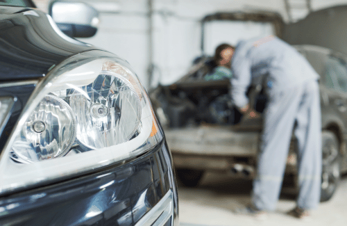 Close-up of a car headlight in an auto repair shop, with mechanics working in the background