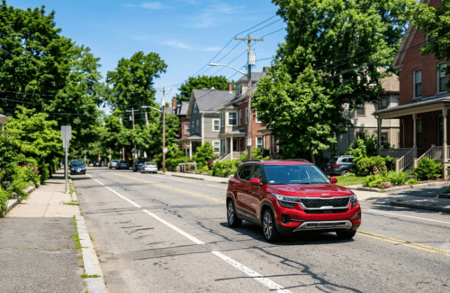 Red SUV driving through a quiet residential neighborhood lined with mature trees and homes. 