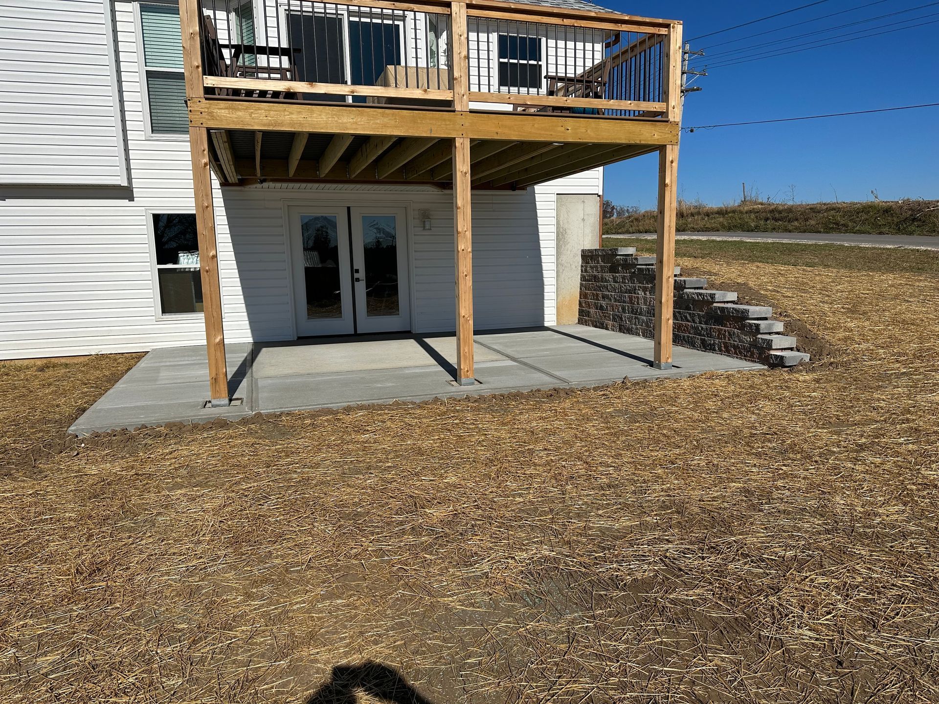Backyard deck with stairs over a concrete patio beside a white house on a grassy lot.
