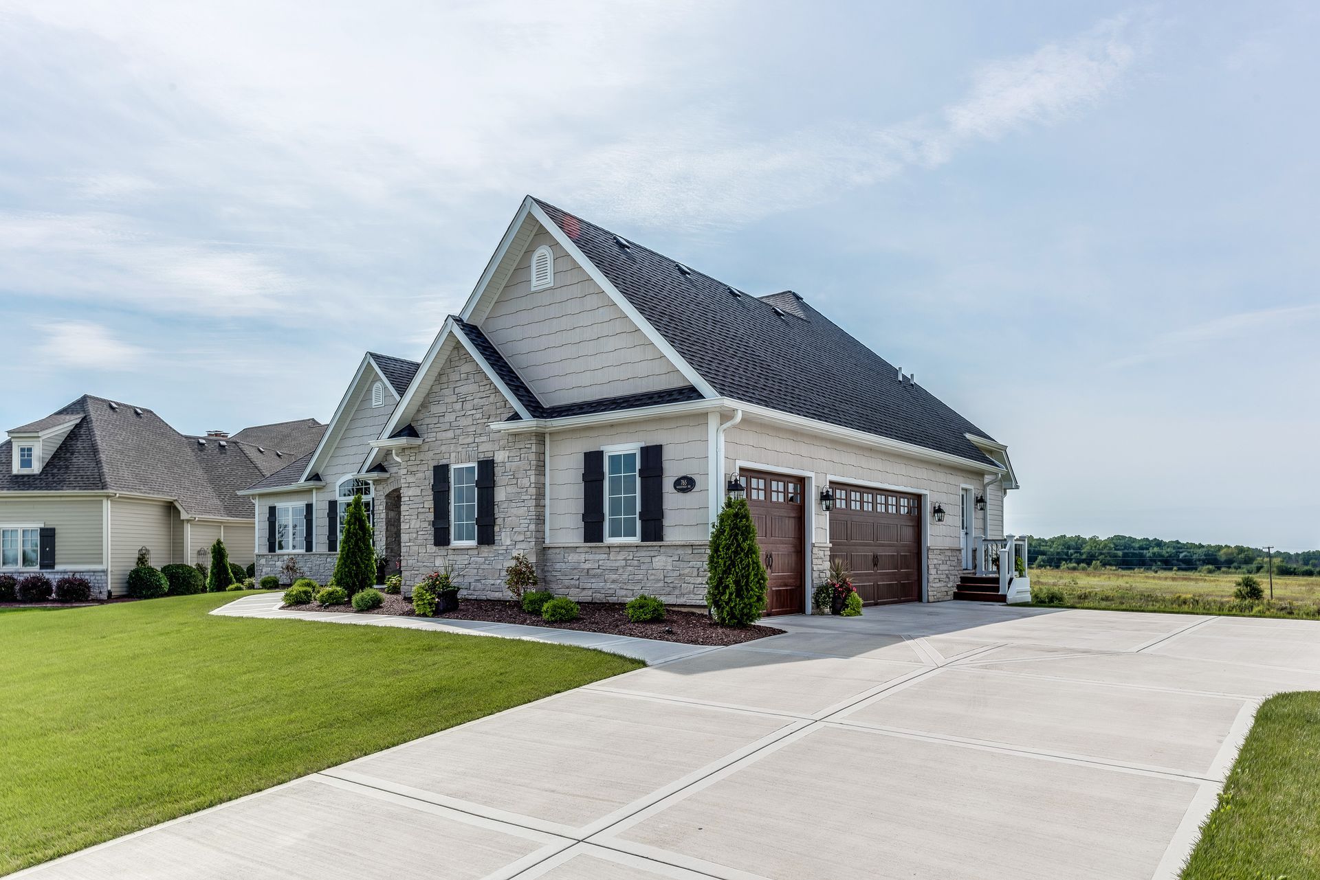 Gorgeous Home With Driveway — St. Charles, MO — TC Concrete Services Modern stone suburban house with gabled roof, two garage doors, and a wide concrete driveway