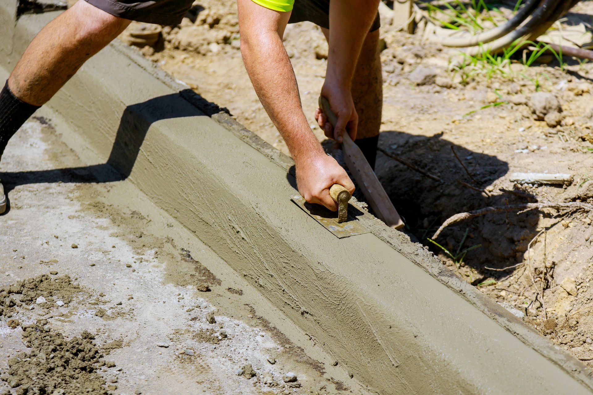 Worker smoothing wet concrete with a trowel beside a curb outdoors