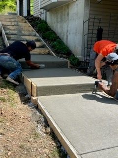 Workers On A Scaffolding — St. Charles, MO — TC Concrete Services Two workers pouring and smoothing a concrete walkway beside stairs and a house