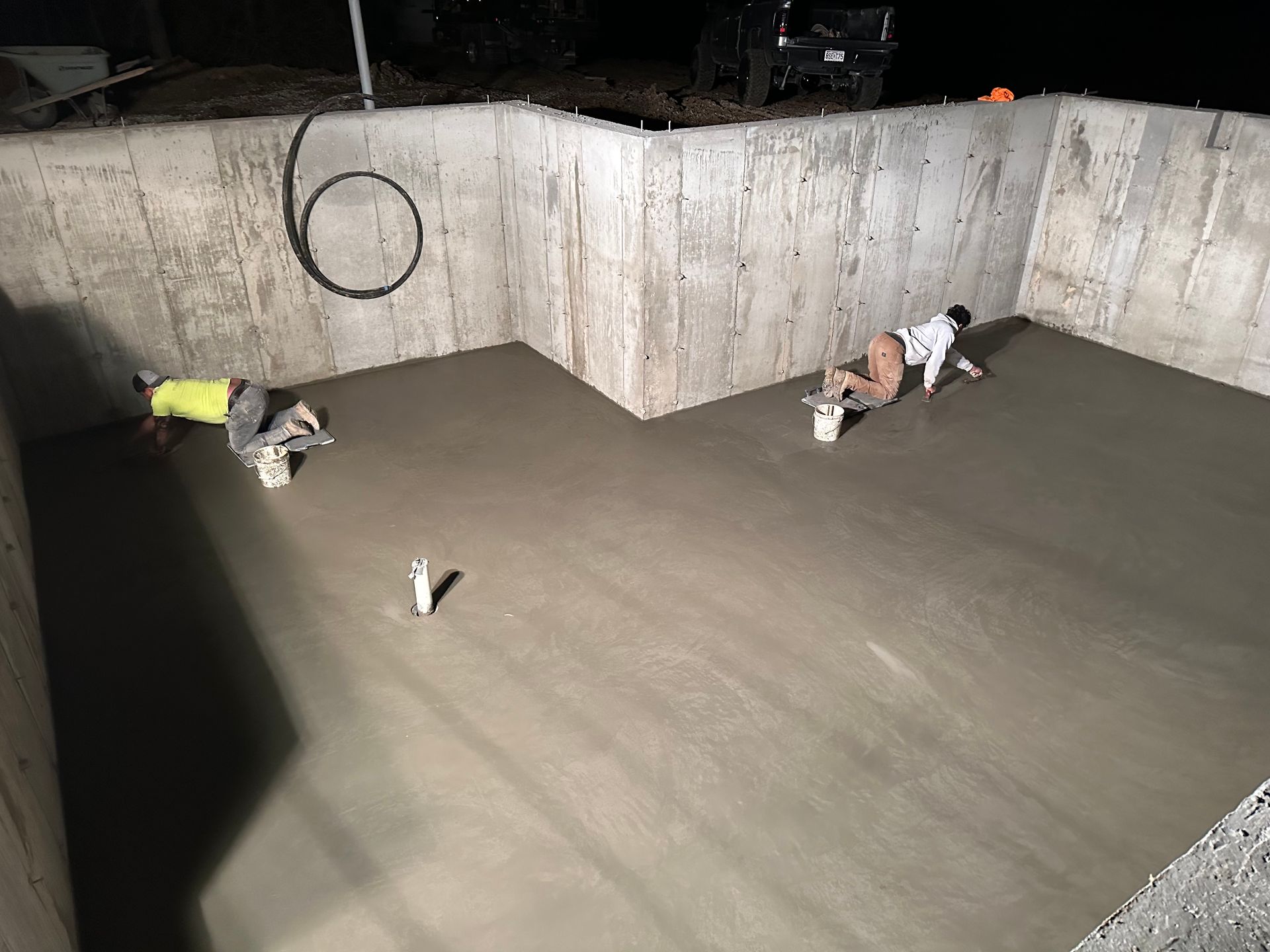 A Concrete Floor Is Being Built On A Construction Site — St. Charles, MO — TC Concrete Services Workers troweling wet concrete in a large foundation pit at night